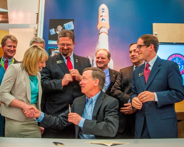 Far left, DigitalGlobe’s Brent Wilson looks over the shoulder of CACI’s Loren Furman as she shakes hands with Governor John Hickenlooper after he signed HB-1178 into law.  Standing, between the Governor and Loren, is Senator Kevin Grantham, a prime sponsor of the bill.  To the far right is House Speaker Mark Ferrandino, also a prime sponsor of the measure.